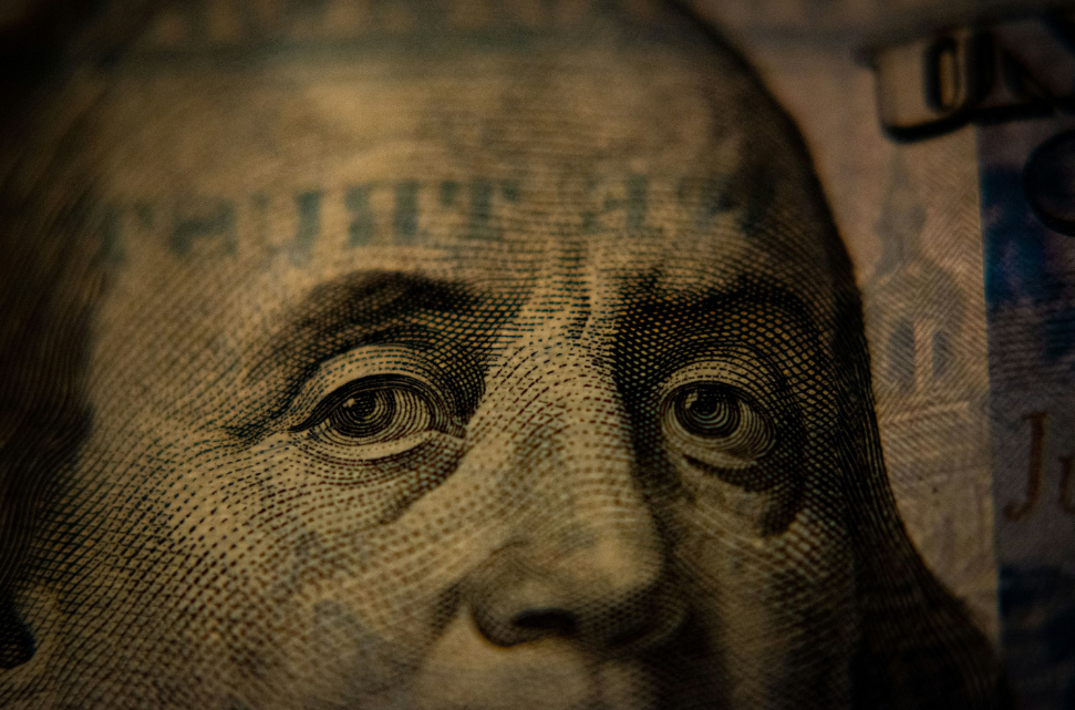 Close-up of a U.S. hundred dollar bill focusing on Benjamin Franklin's eyes, highlighting fine print details related to GDP growth.